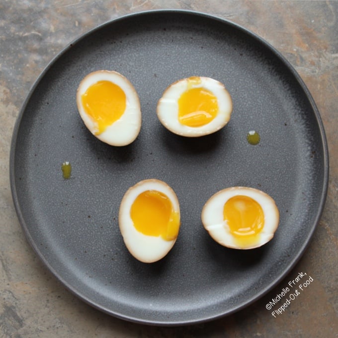 2 Soy-Miso Marinated Ramen Eggs, sliced in half on a grey, circular plate. The white is suffused with a golden-brown color from the marinade, while the yolks are perfectly custardy.