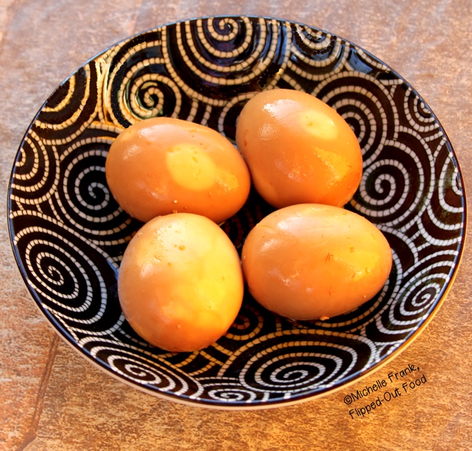 4 Asian-Inspired Dishes, #4: Soy-Miso Marinated Ramen Eggs by Flipped-Out Food. 4 ramen eggs sit in a decorative black and white bowl. The marinade has turned the eggs a deep, golden brown.