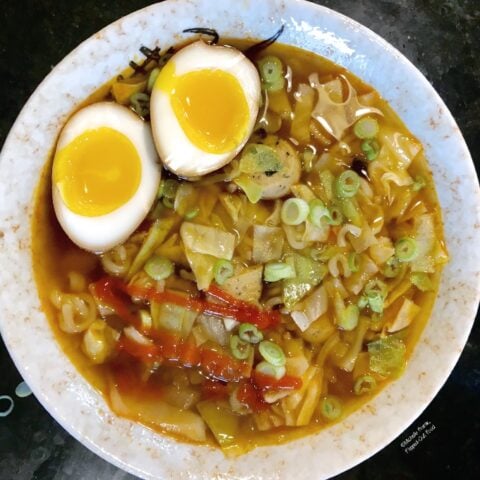 A bowl of ramen soup garnished with 2 halves of a custardy soy-miso marinated egg. The soup is also garnished with scallions and sriracha.