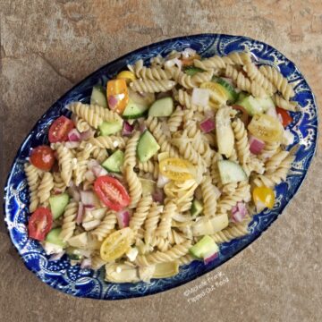 Easy Greek Pasta Salad in an oval, bright blue, ornamental serving bowl.