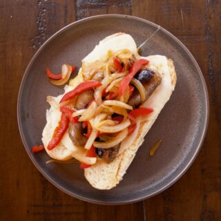 Grilled Italian Sausage Sandwiches with Pepper-Onion Foil Packs on a grey plate sitting atop a dark wood table.