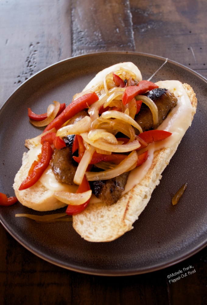 Side view of a Grilled Italian Sausage Sandwich with Pepper-Onion Foil Packs on a grey plate sitting atop a dark wood table.