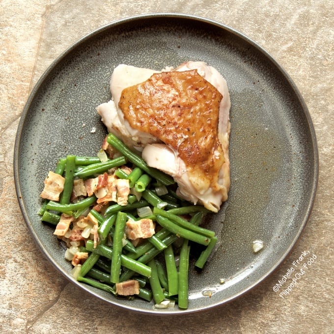 Overhead view of Green Beans with Bacon and Onions on a grey plate with a grilled chicken thigh.