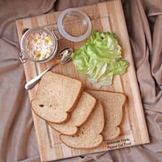 Tangy Deviled Ham & Cheese Spread in a small jar sits on a cutting board along with slices of wheat bread and lettuce.