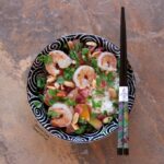 Top view of a black bowl with white swirls, filled with Shrimp Thai Basil Stir-Fry. Dig in with the ornate chopsticks sitting on top of the bowl.
