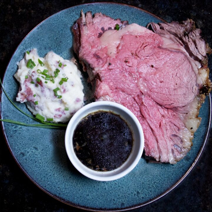 Easy Skin-On Mashed Potatoes with Horseradish, garnished with minced chives on a plate with a gigantic slab of prime rib with au jus.
