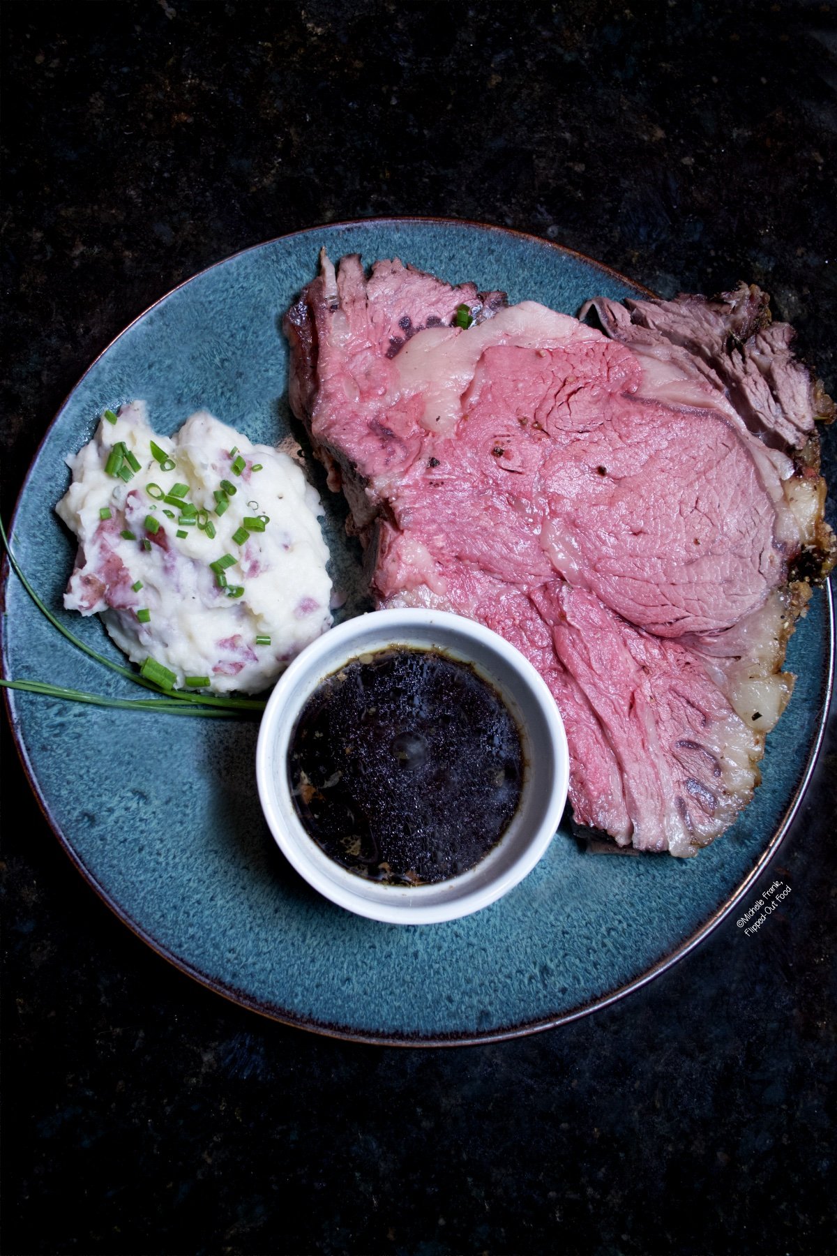 Slice of prime in rib and horseradish mashed potatoes served on plate accompanied with au jus in a small white ramekin.