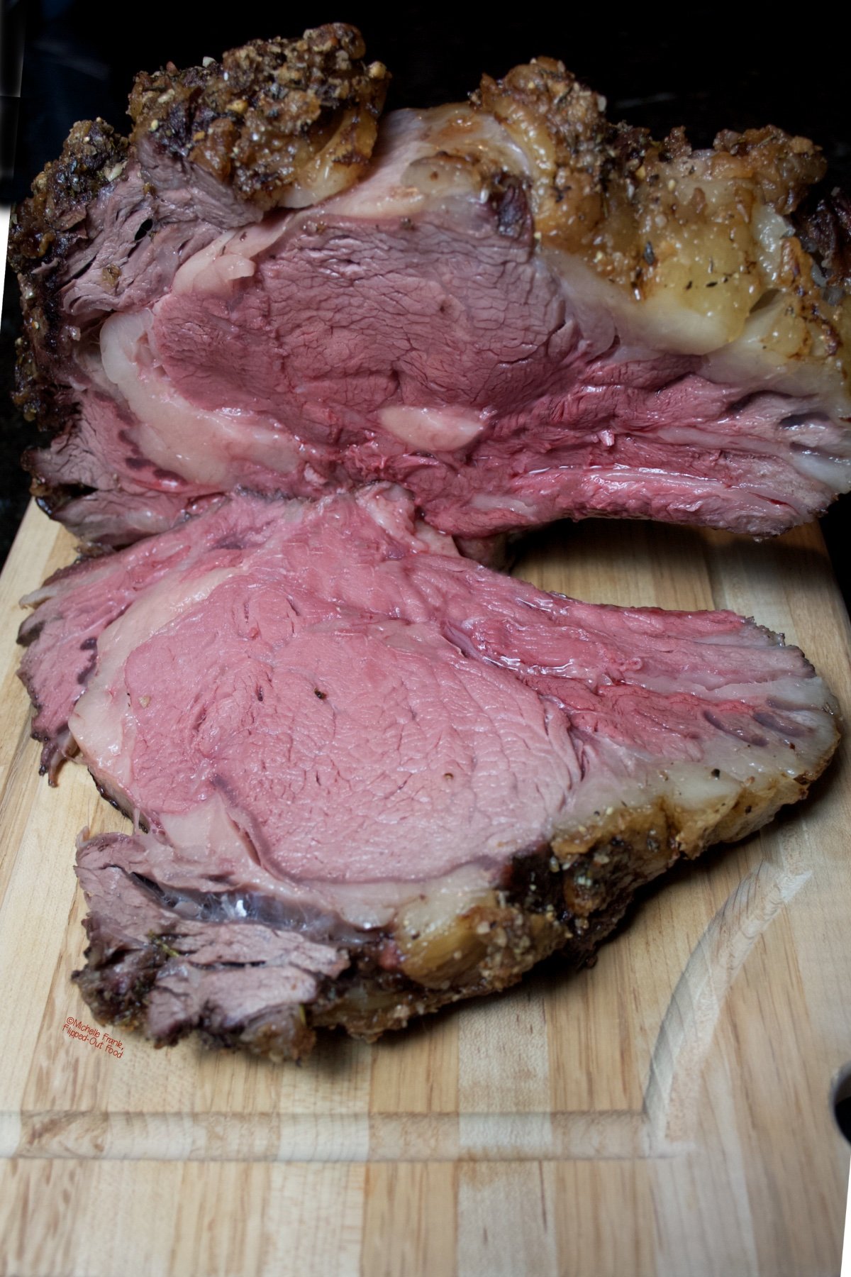 Date Night Prime Rib Roast on a wooden cutting board, with a single slab sliced off and laying on the board.