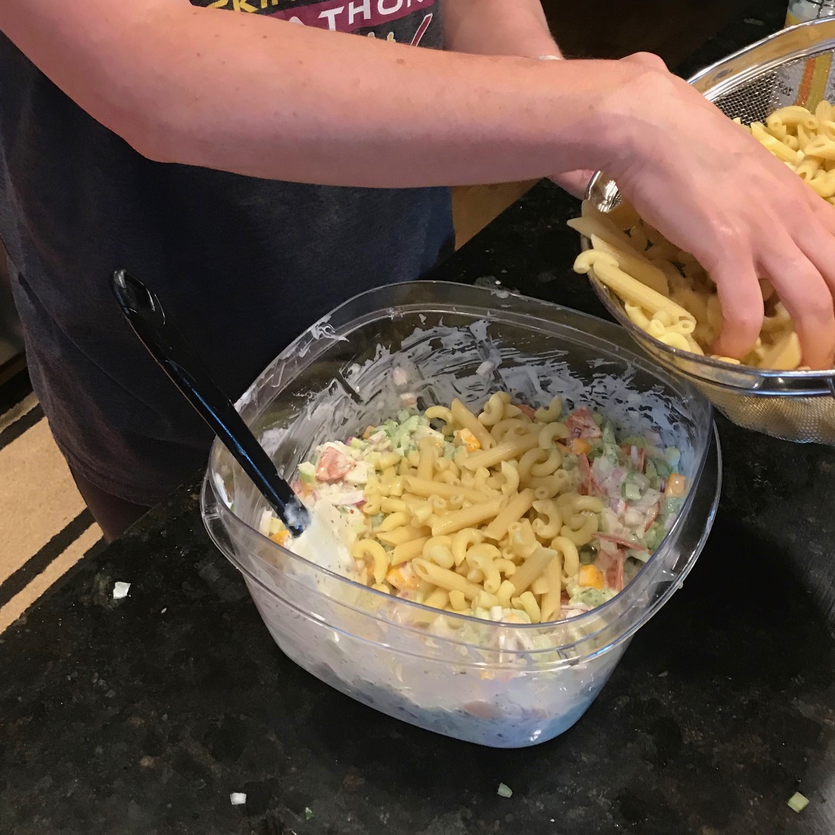 image showing cooked pasta being added to vegetable cheese pasta salad dressing mixture.