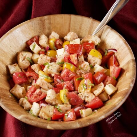 Side-view of Summer Panzanella Salad in a wooden serving bowl with a serving spoon.