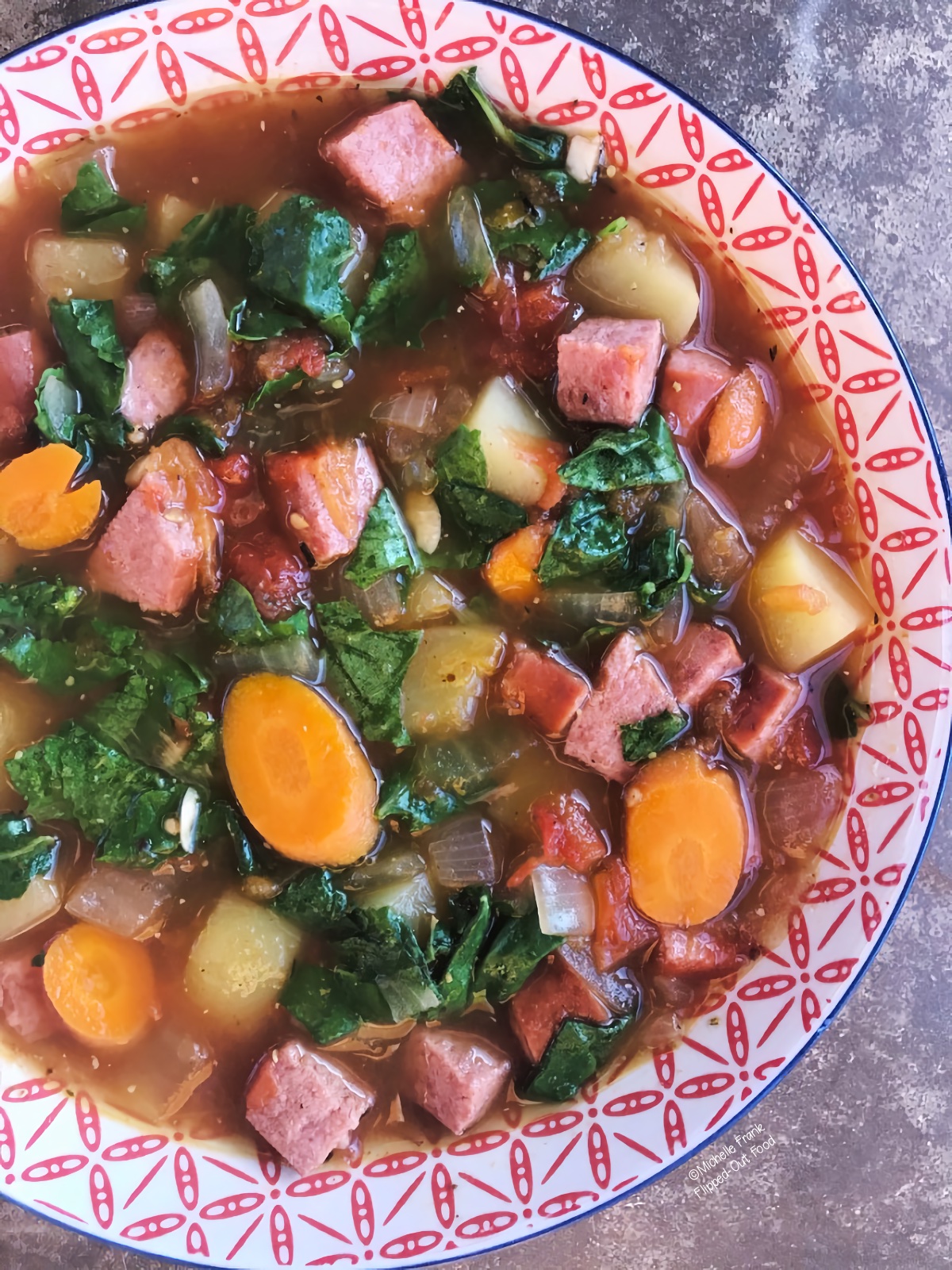 Close-up of a serving of Sausage Kale and Potato Soup in a decorative red and white bowl.