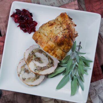 Turkey Roulade with Sausage Stuffing on a white platter garnished with sage and cranberry sauce