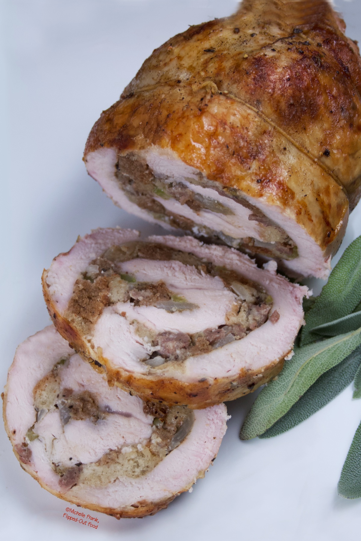 Close-up of a Turkey Roulade with Sausage Stuffing, with two sliced pieces on a platter garnished with sage.