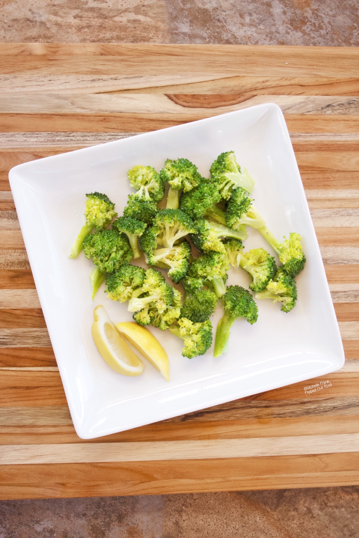 Easy Microwave Broccoli on a white plate with lemon wedges.