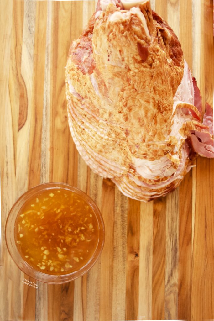 Orange-Bourbon ham glaze sitting next to an as-yet unglazed, spiral-sliced ham.