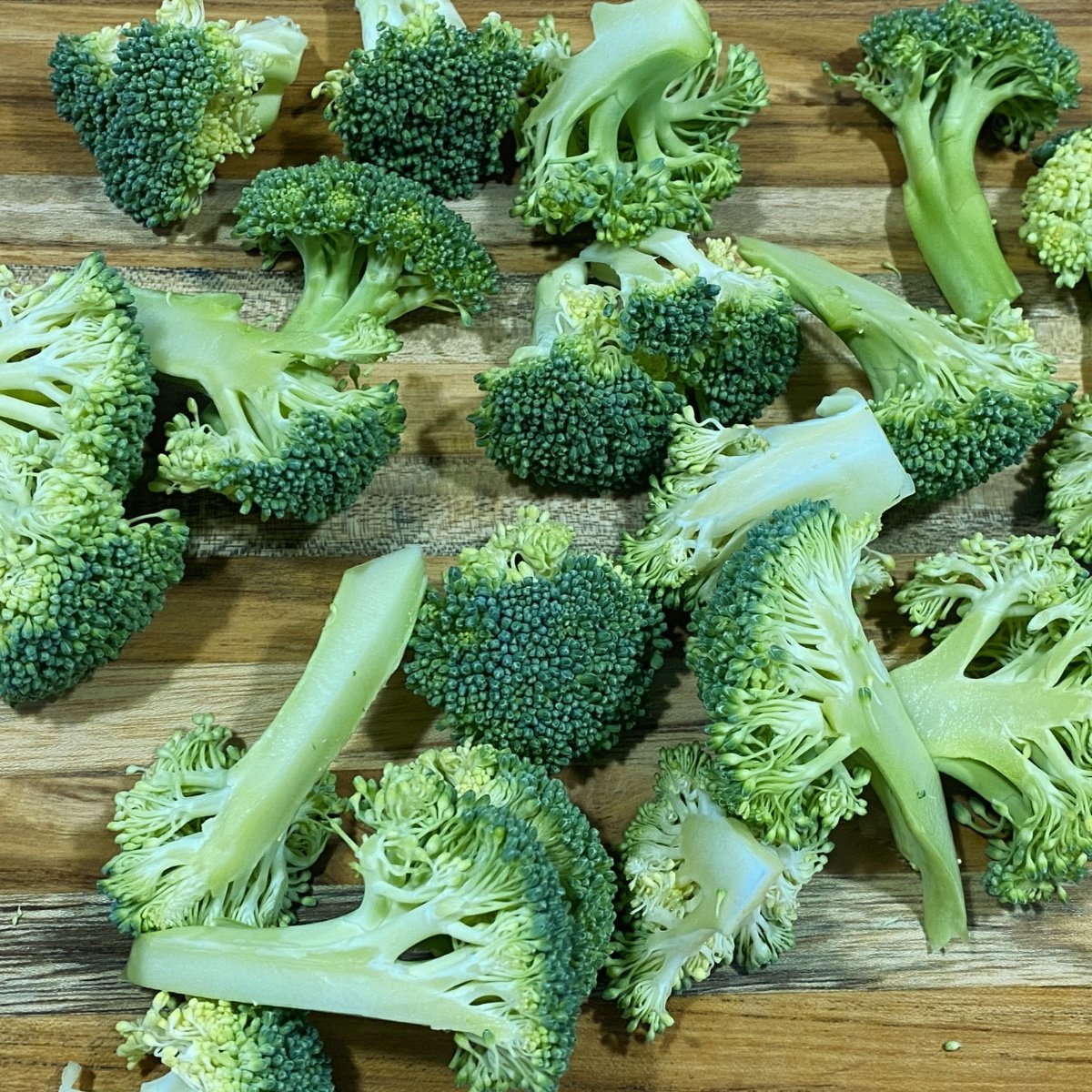 Prepped broccoli florets on a wooden cutting board.