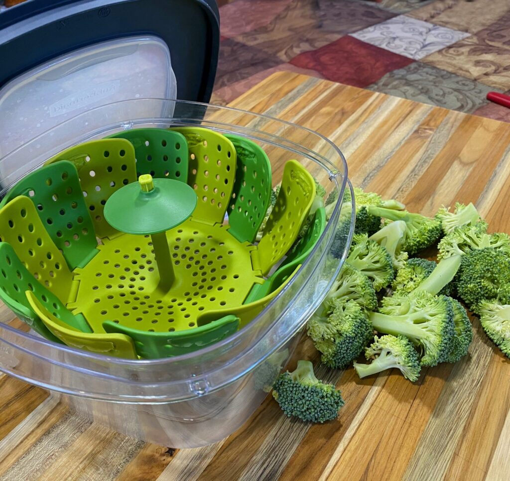 Easy Microwave Broccoli steamer setup: a microwave-safe container with a lid, a silicone colander set inside, and an inch of water added to the bottom.