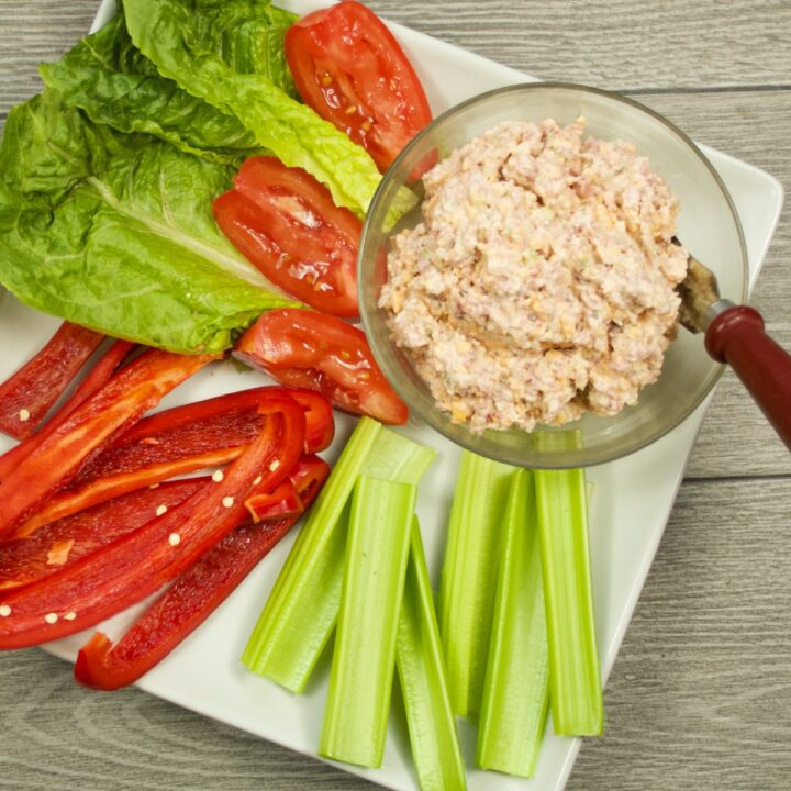 Keto Ham Salad Spread in a bowl on a white serving platter with celery sticks, sliced red pepper and tomato, and lettuce leaves.