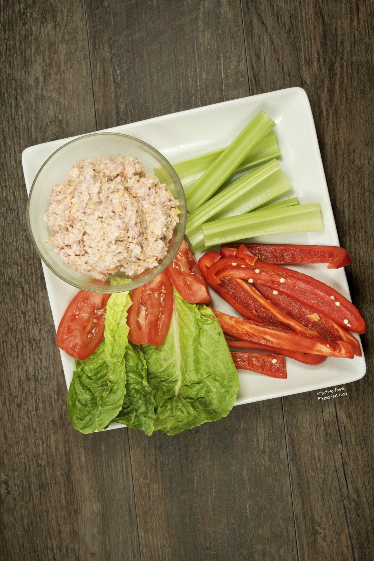 Top view of Keto Ham Salad in a serving bowl set onto a plate with celery sticks, red pepper strips, Romaine lettuce, and tomatoes.