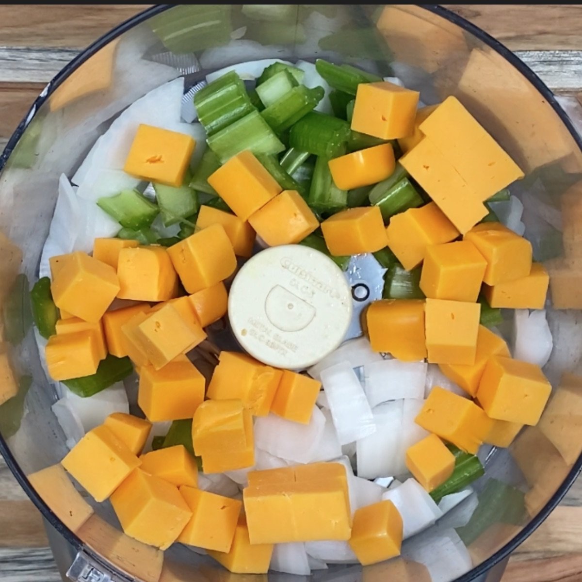 Overhead view of onion, celery, and cheese in the food processor awaiting to be processed.