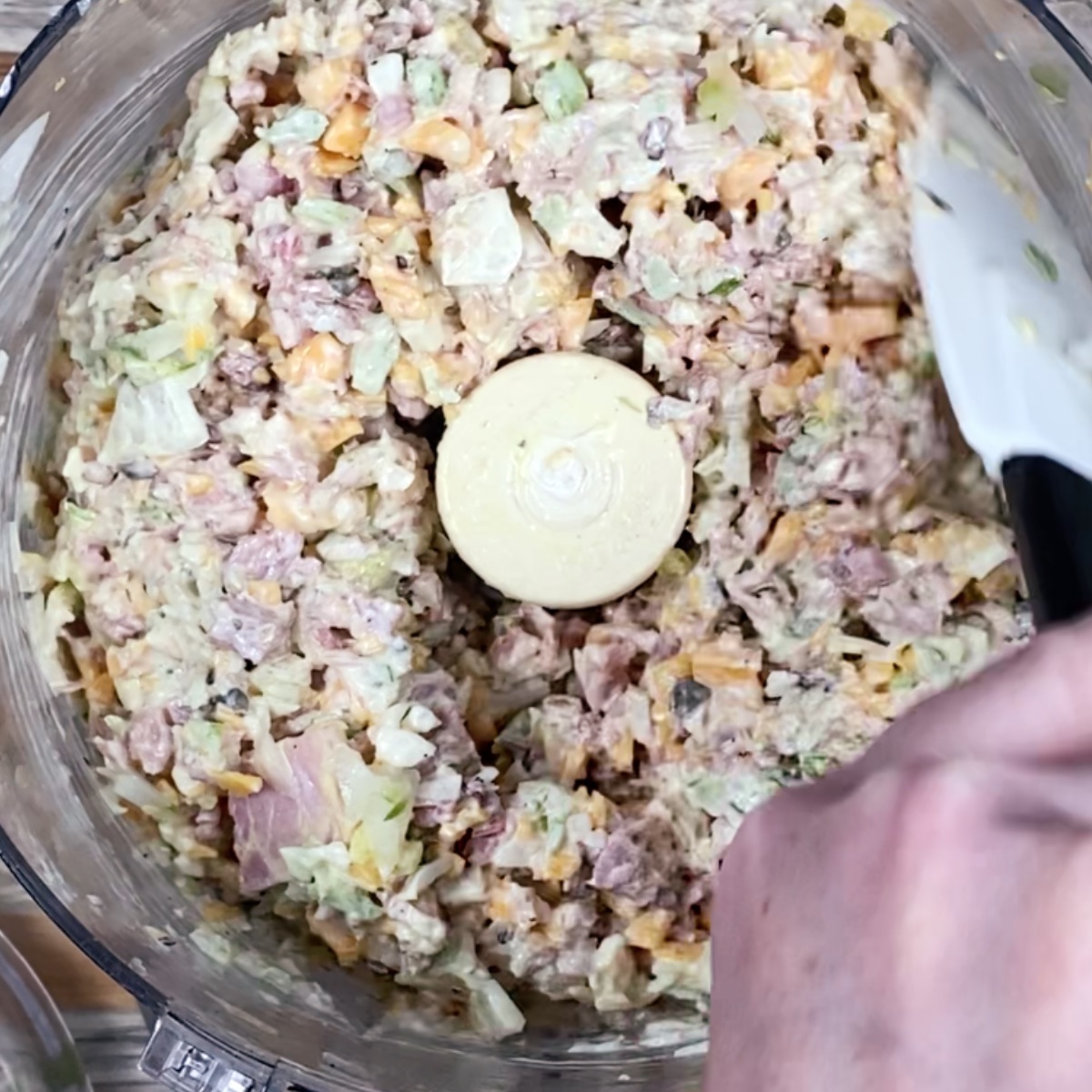 Overhead view showing how to scrape down the sides of the food processor half way through pulsing the ham salad ingredients.