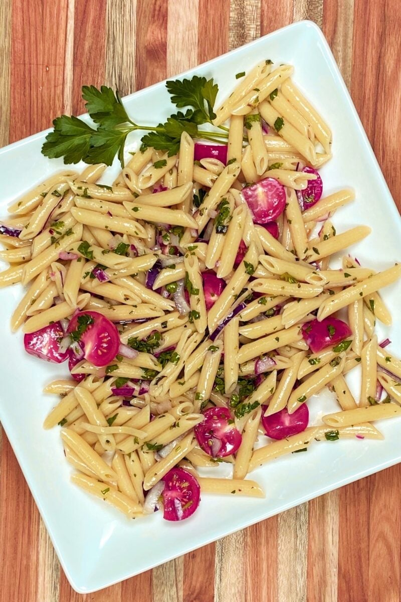 The finished Chimichurri Pasta Salad on a white platter set atop a teak cutting board.