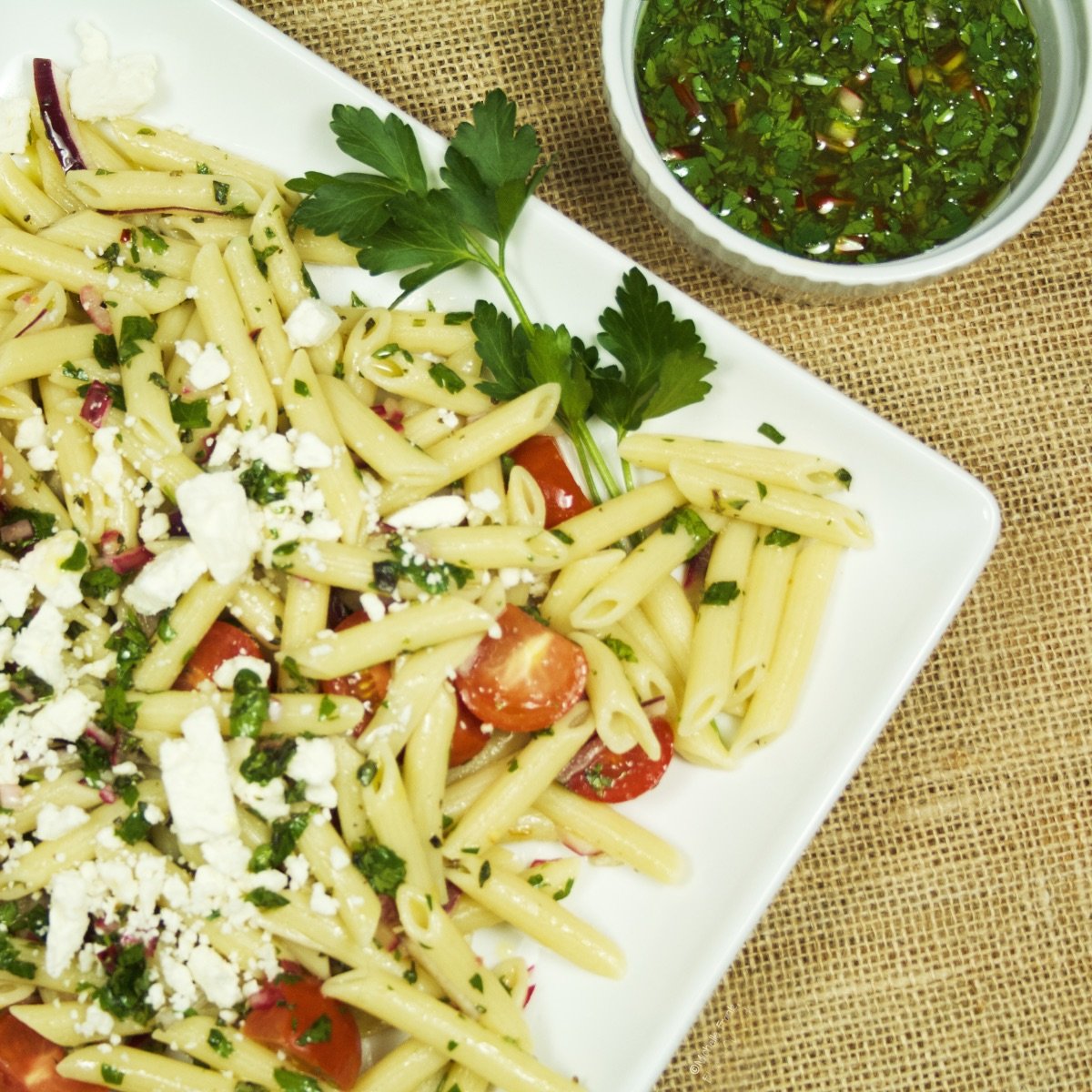 Closeup of a platter full of Chimichurri Pasta Salad sitting next to a ramekin of chimichurri sauce.