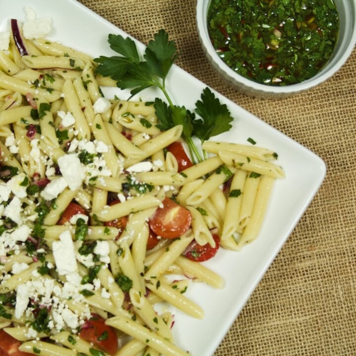 Chimichurri Pasta Salad on a white platter, sitting next to a ramekin of chimichurri sauce.