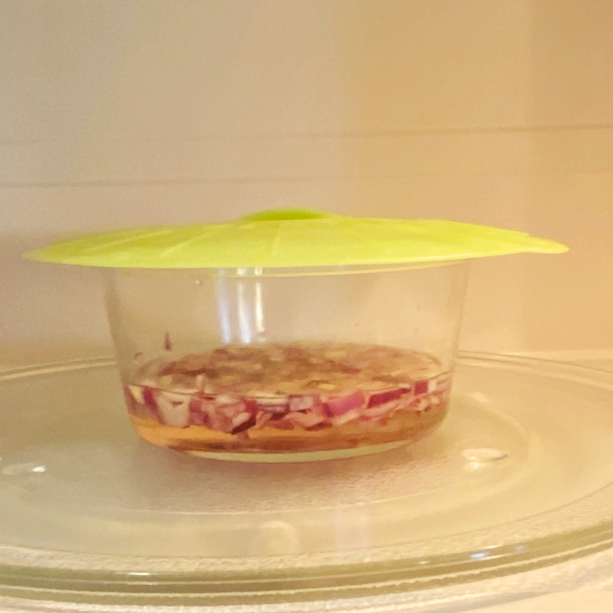 A loosely lidded bowl with red onion and vinegar in the microwave, ready to make pickled red onion.