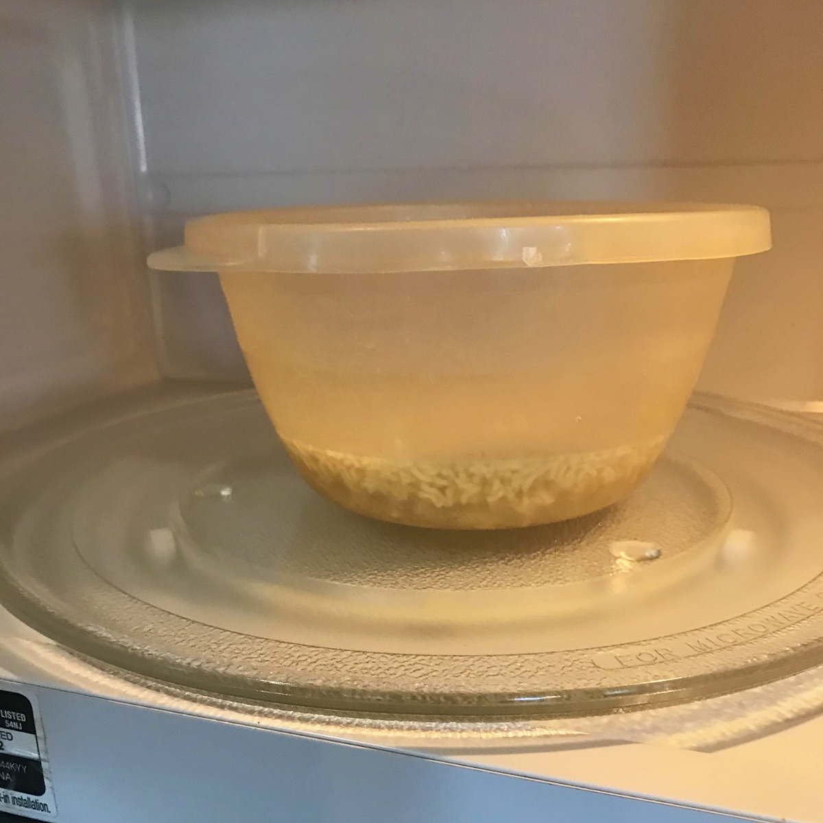 SIde view showing crushed ramen noodles in a microwave-safe bowl, covered with water inside the microwave about to be heated up.