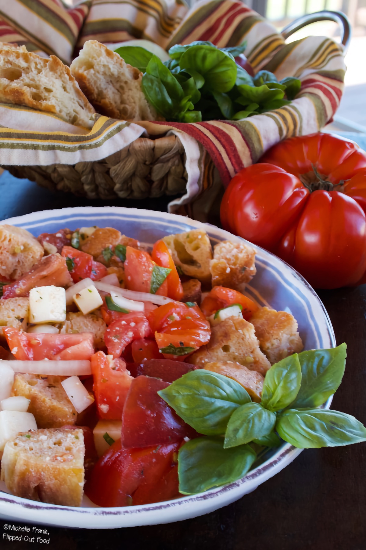 Summer Panzanella Salad garnished with a sprig of basil. An heirloom tomato sits in the background.