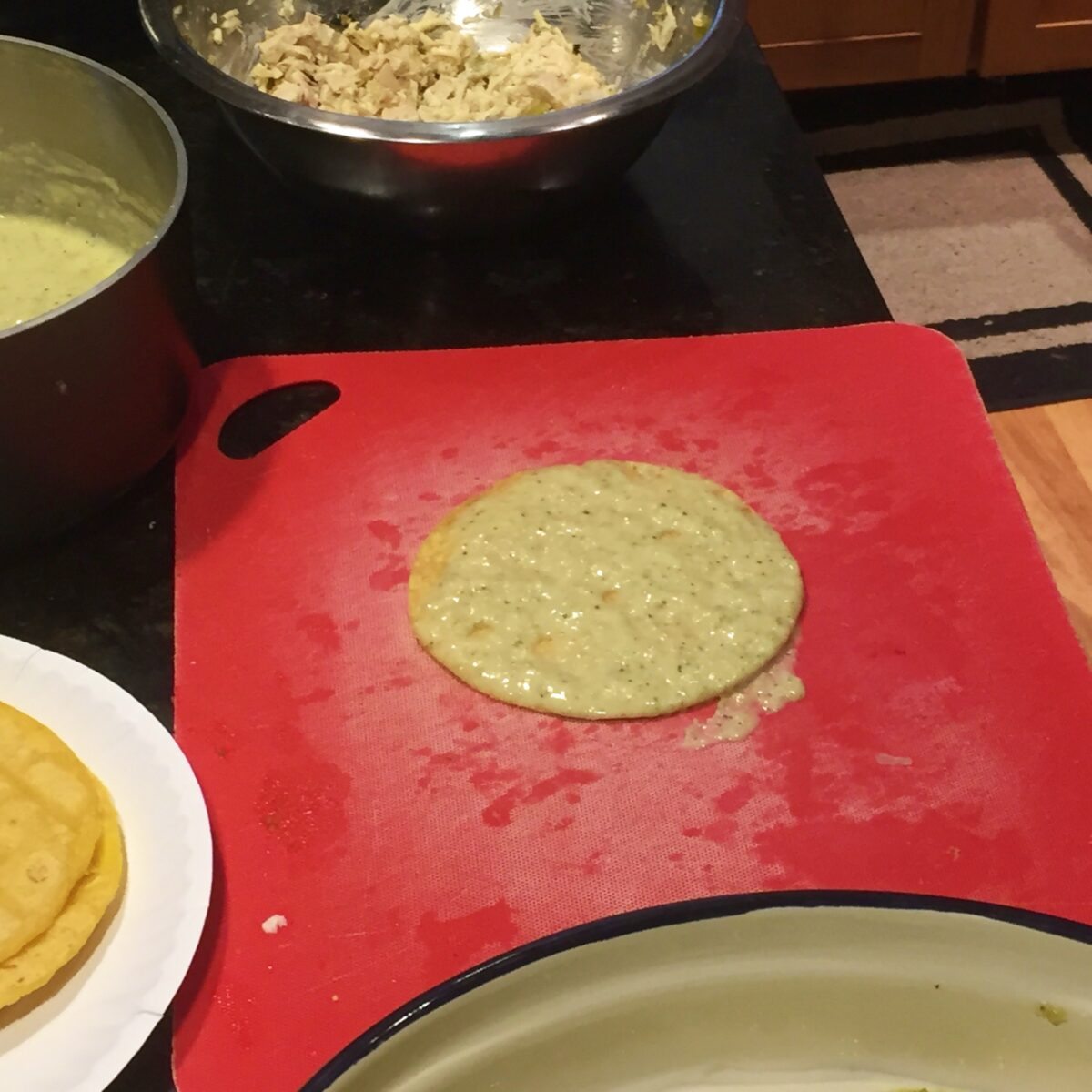 A corn tortilla with one side covered in creamy green chile enchilada sauce on a cutting board, ready for adding enchilada filling.