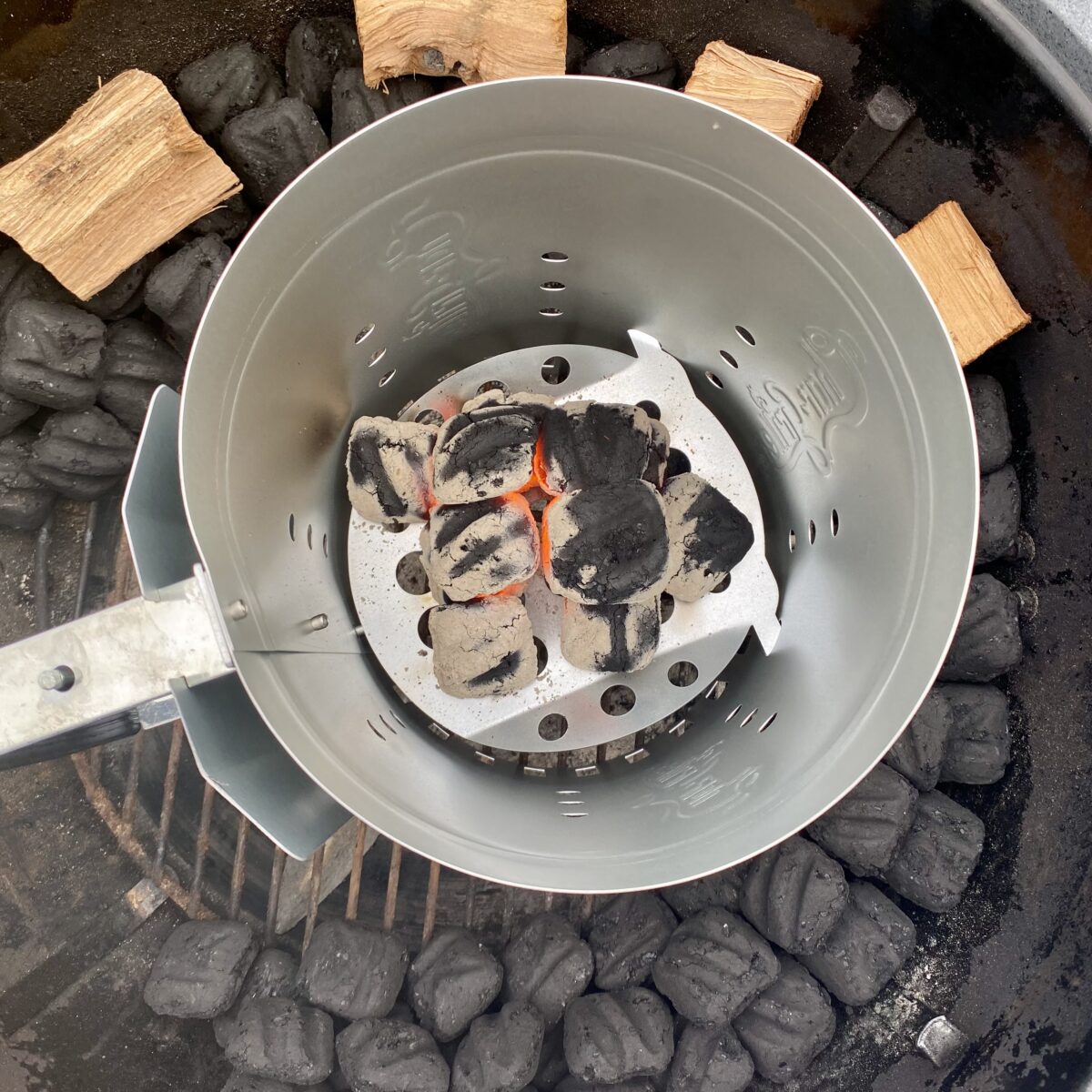 Overhead view showing 12 hot coals in a chimney starter that are ready to be placed at the head of the snake of unlit coals.