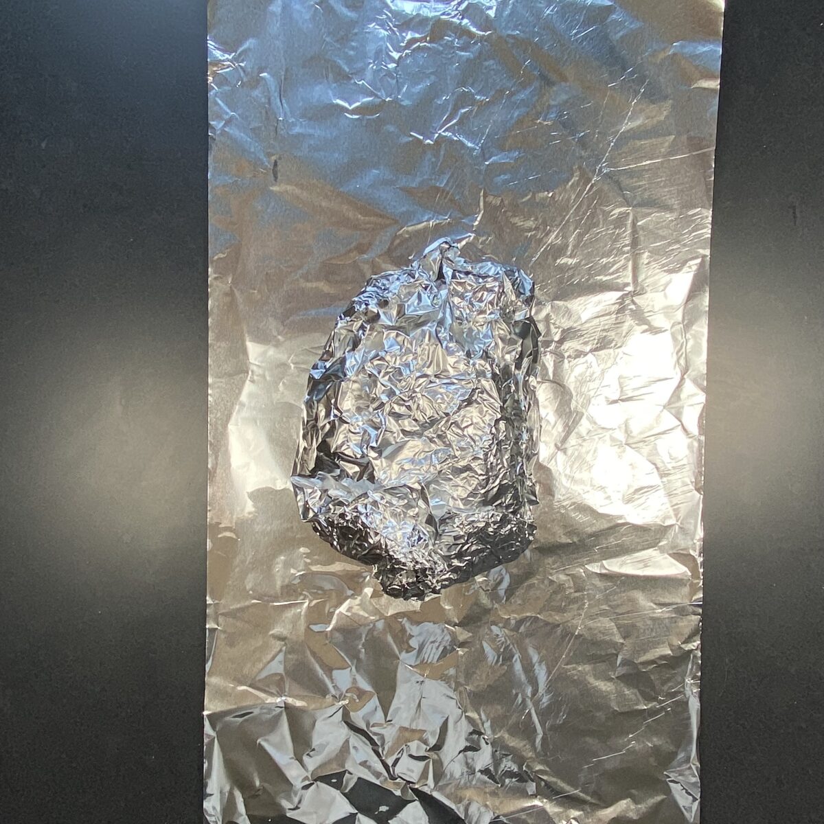 Top view of smoked pork butt wrapped in first layer of tinfoil showing the direction of how to wrap second layer of tinfoil