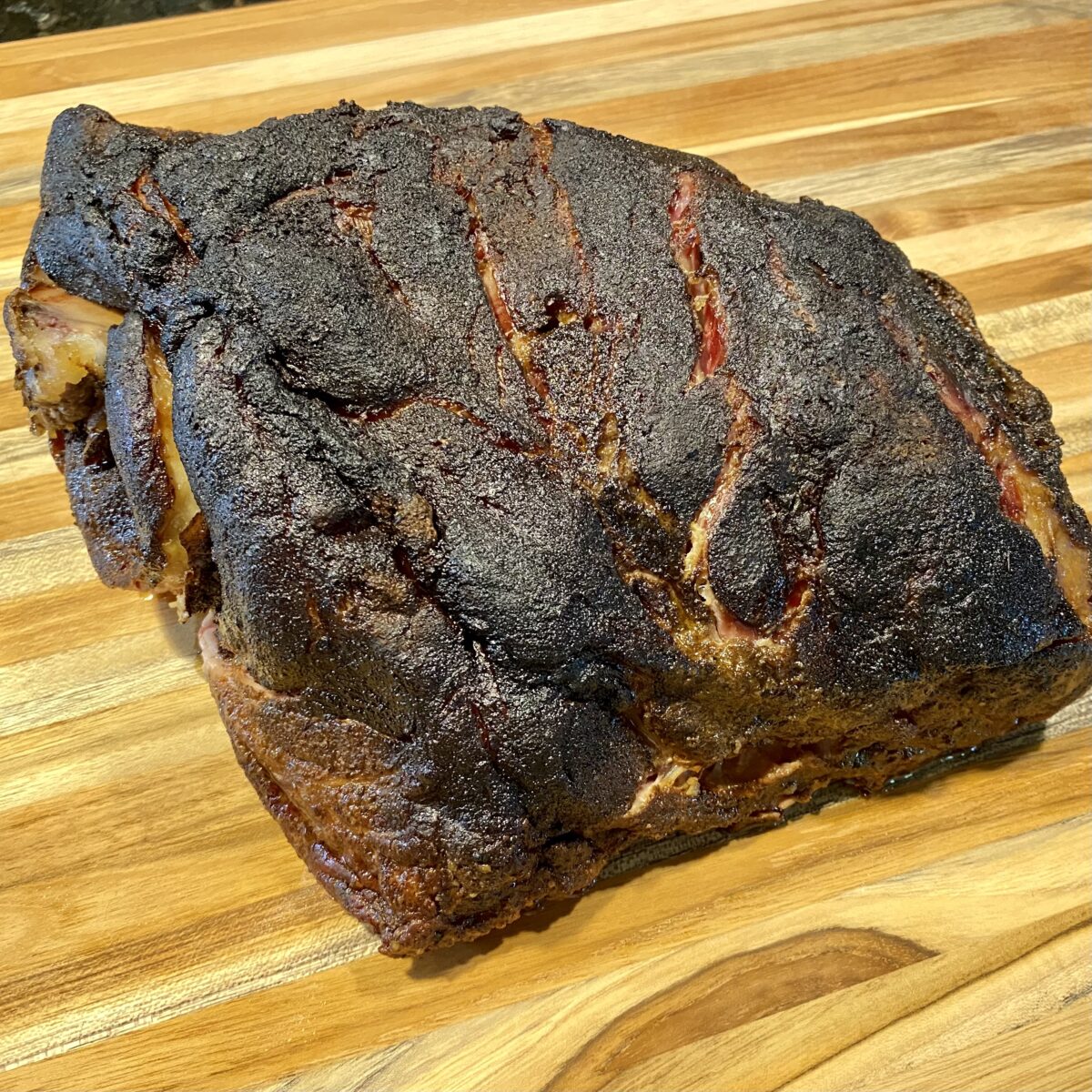 Top view of smoked pork butt resting on a wooden cutting board about to be pulled into pulled pork.