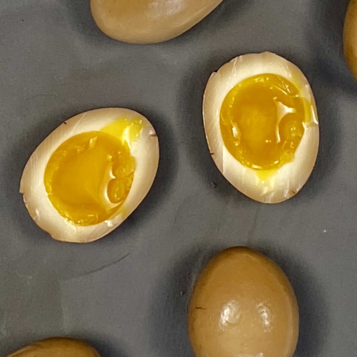 top view of soy-miso marinated ramen egg, cut in half showing runny yolk and deep marinade penetration placed on a gray plate.