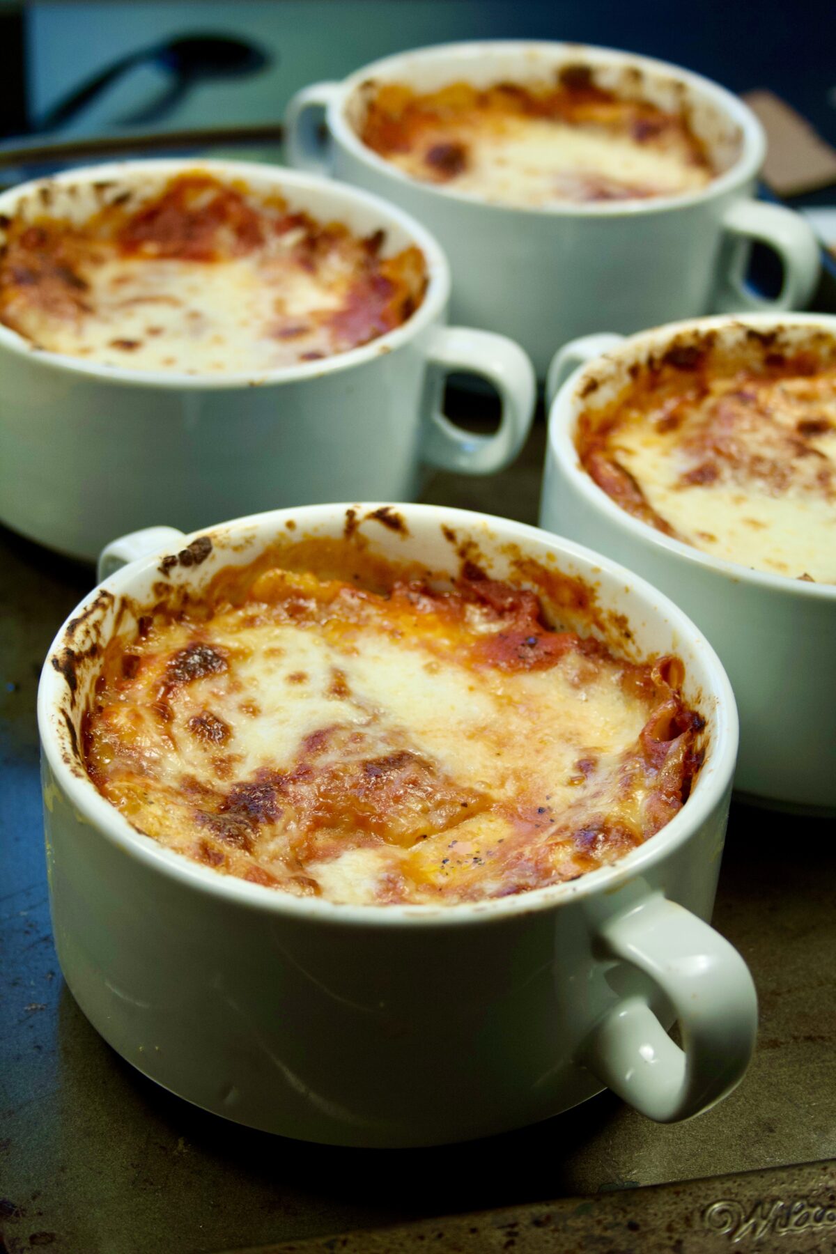 Side view of four freshly baked lasagna bowls positioned on counter.