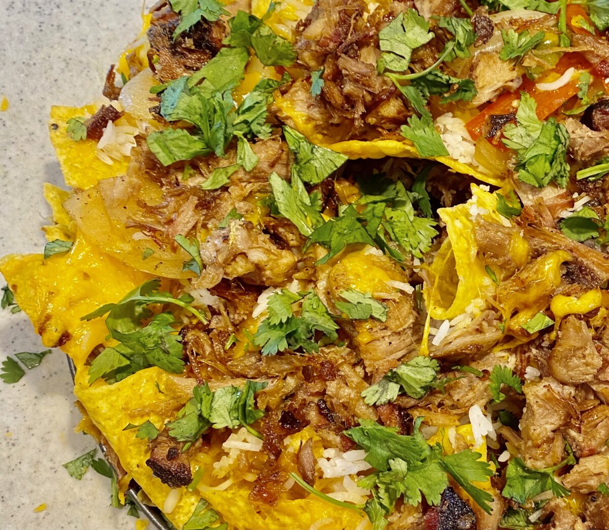 Close up top view of pulled pork nachos topped with cilantro, melted cheese, and fajita vegetables.