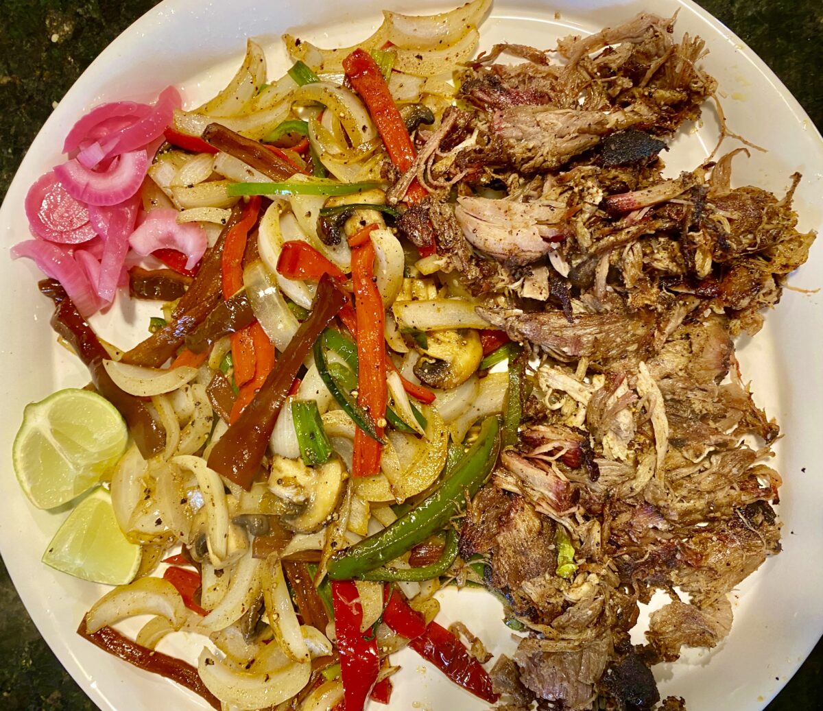 Top view of seared mexican flavored pulled pork along side fajita vegetables on a large white serving platter.