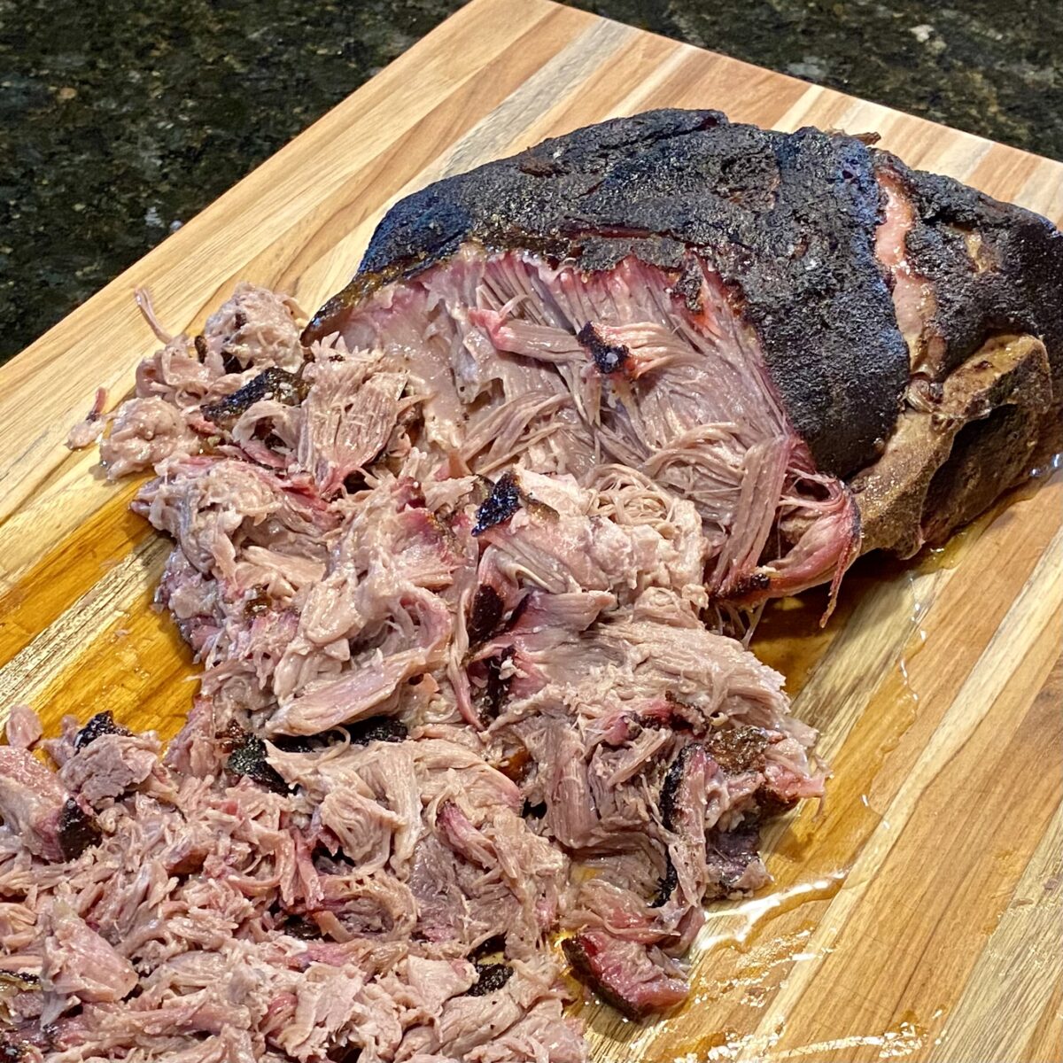 Side view of smoked pork butt that that has been partially pulled positioned on a cutting board.