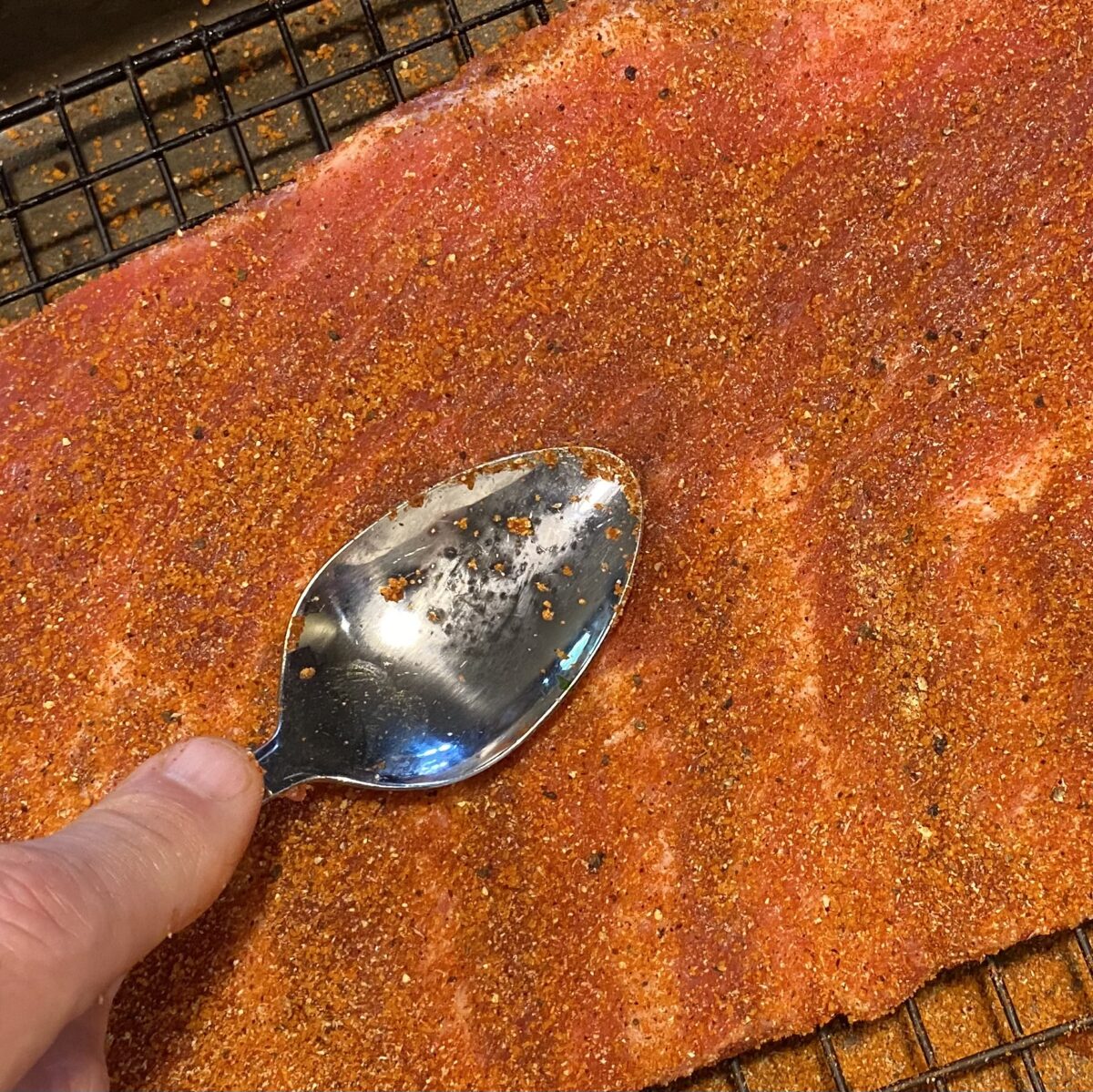 Top view showing the back of a spoon pressing the pork butt rub into the pork butt.