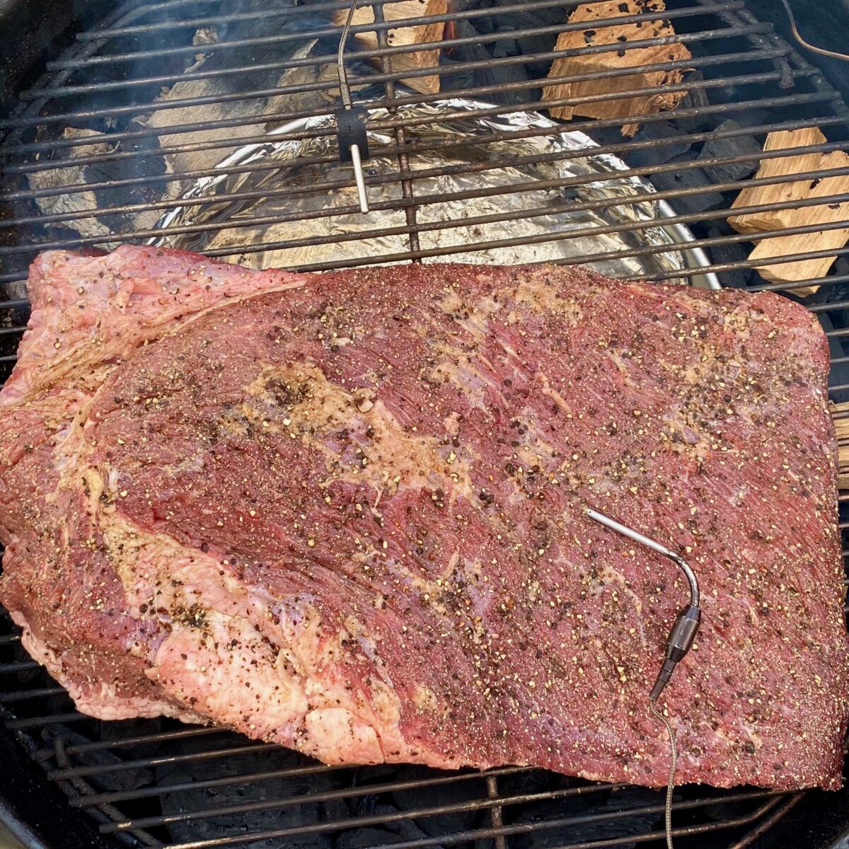 Top view of rubbed brisket just placed on a charcoal grill to be smoked.