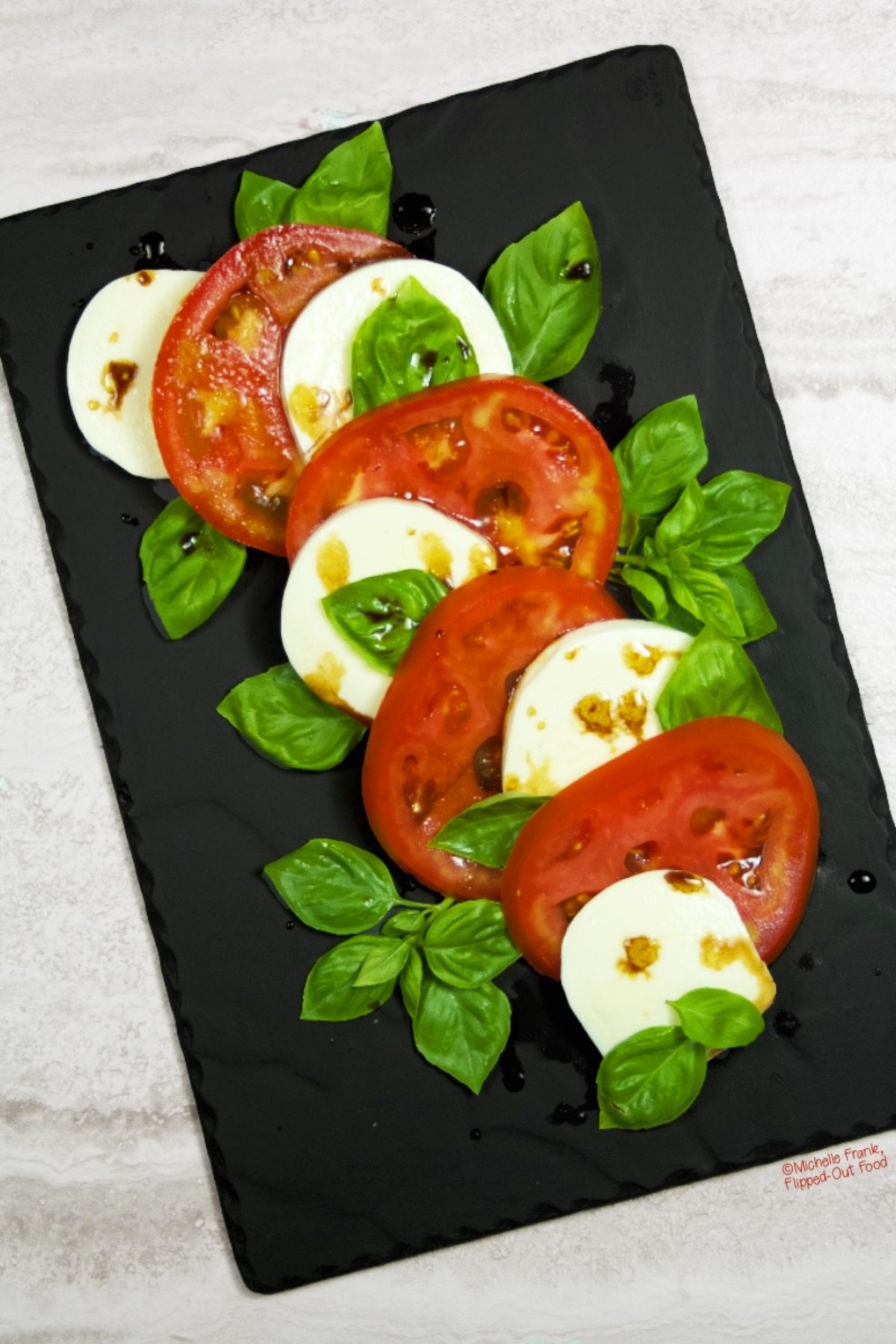 A whimsically arranged Caprese Salad with Balsamic Glaze on a slate platter.