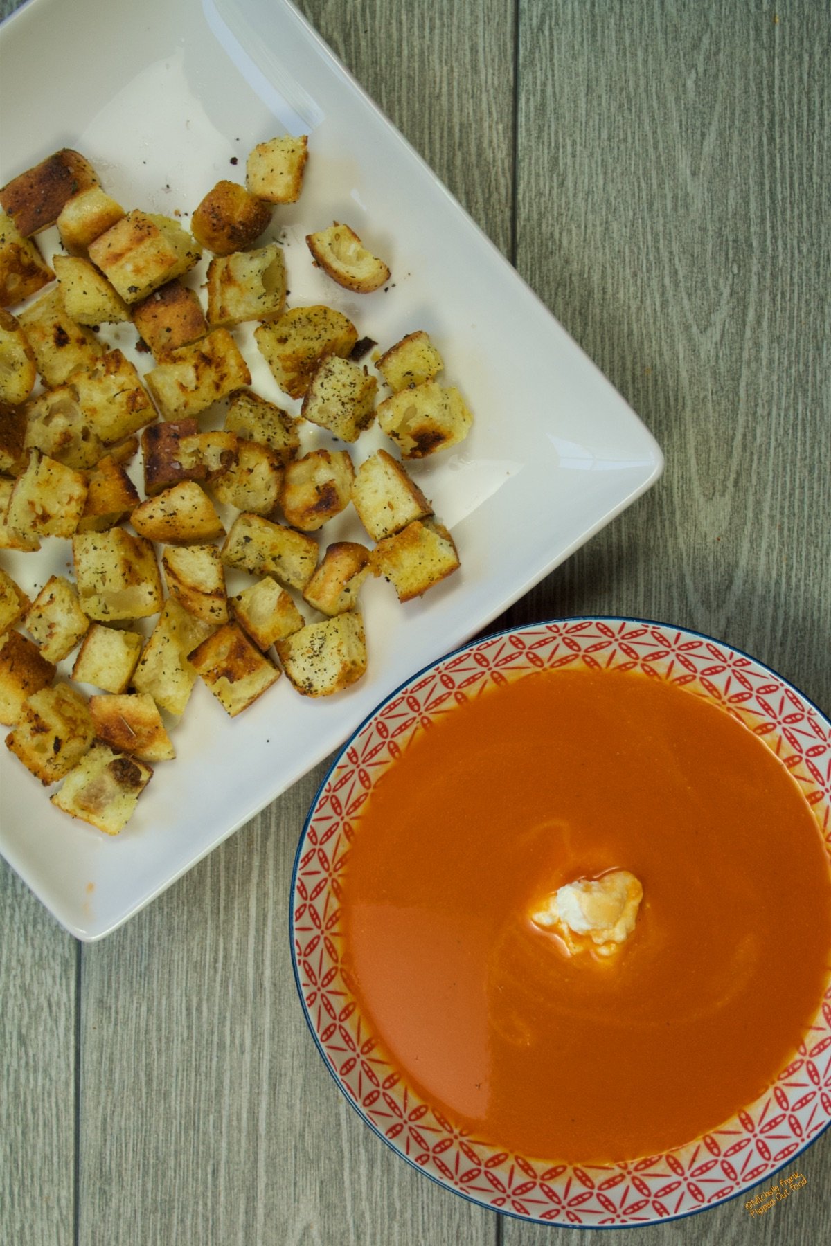 A plate of freshly made Easy Stovetop Croutons on a white plate sitting next to a bowl of fresh tomato soup.