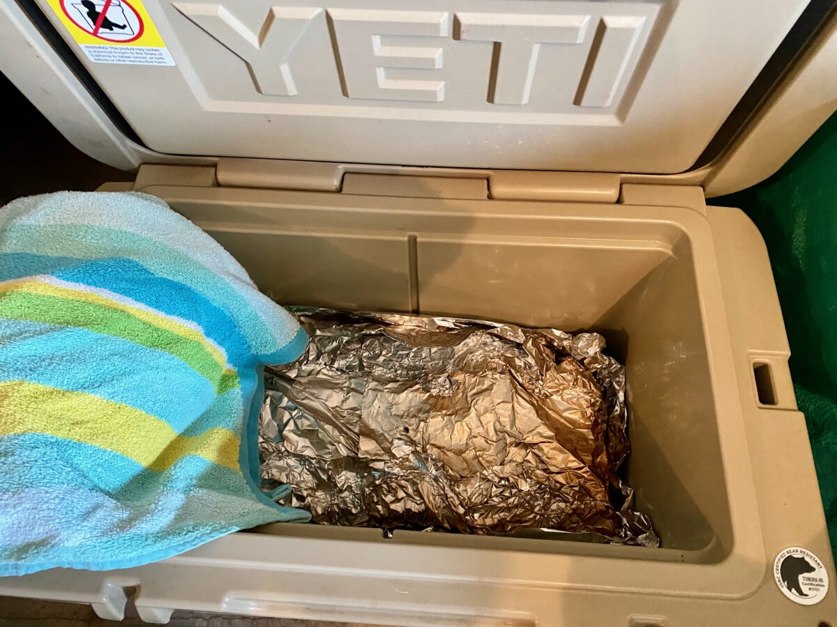 Top view of wrapped smoked brisket placed into a cooler to rest until it is time to slice and serve.