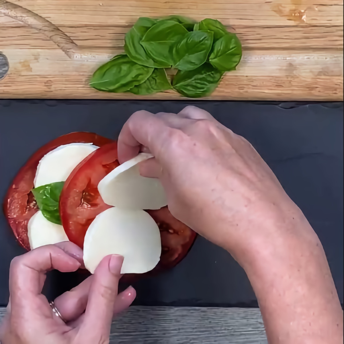 Assembling the Caprese Salad by alternating layers of tomato, mozzarella, and basil.
