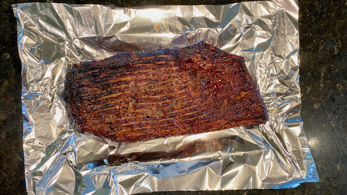 Top view of smoked brisket placed into aluminum foil about to be wrapped.