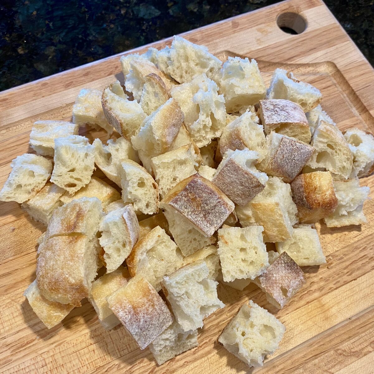 Side view freshly cut bread cubes cut into one inch pieces on a wooden cutting board.