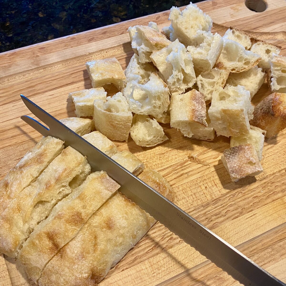 Side view of a knife cutting crunchy bread into one inch bread cubes. 