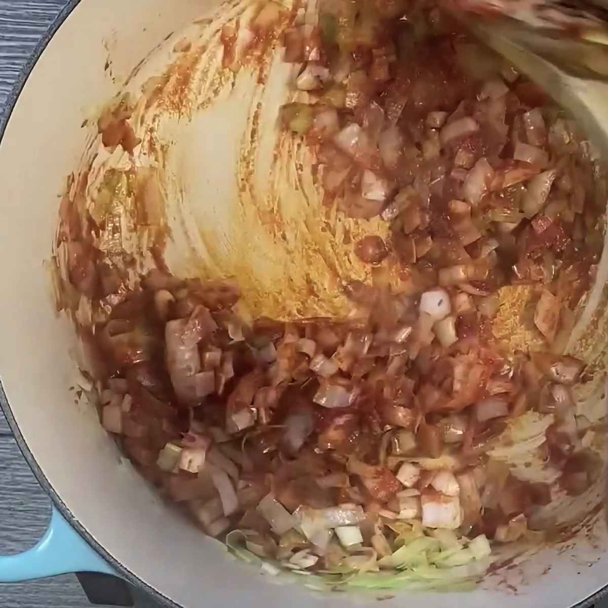 Top view of dutch oven caramelizing tomato paste mixed with leeks and onions.